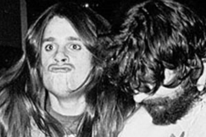 Ozzy Osbourne makes a duck face while kicking up one of his legs and gripping onto his band mate.