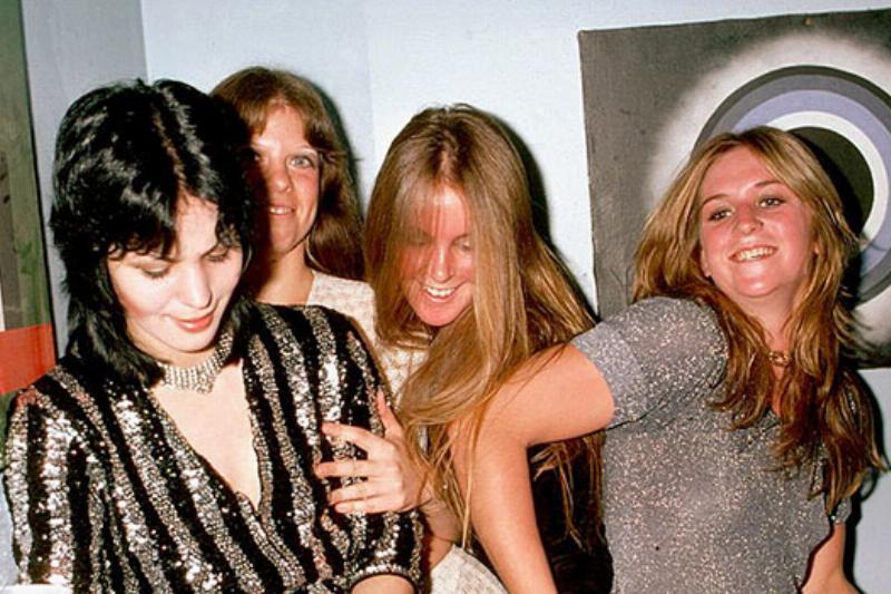 Four members of the runaways fall into one another while smiling backstage.