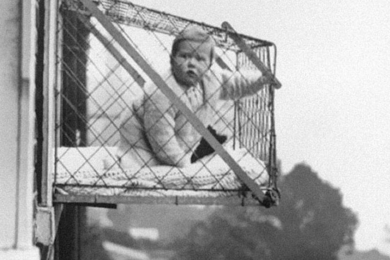 baby in cage bed hanging out window of apartment