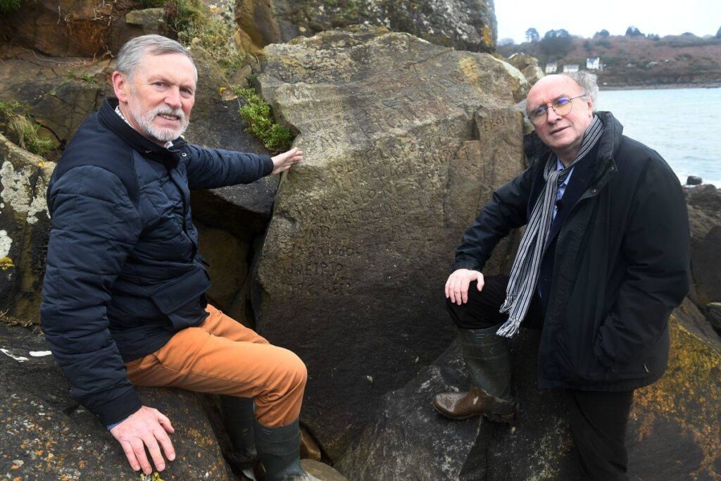 Frenchmen Robert Faligot (R) and Noel Rene Toudic pose near the inscripted rock they unscrambled