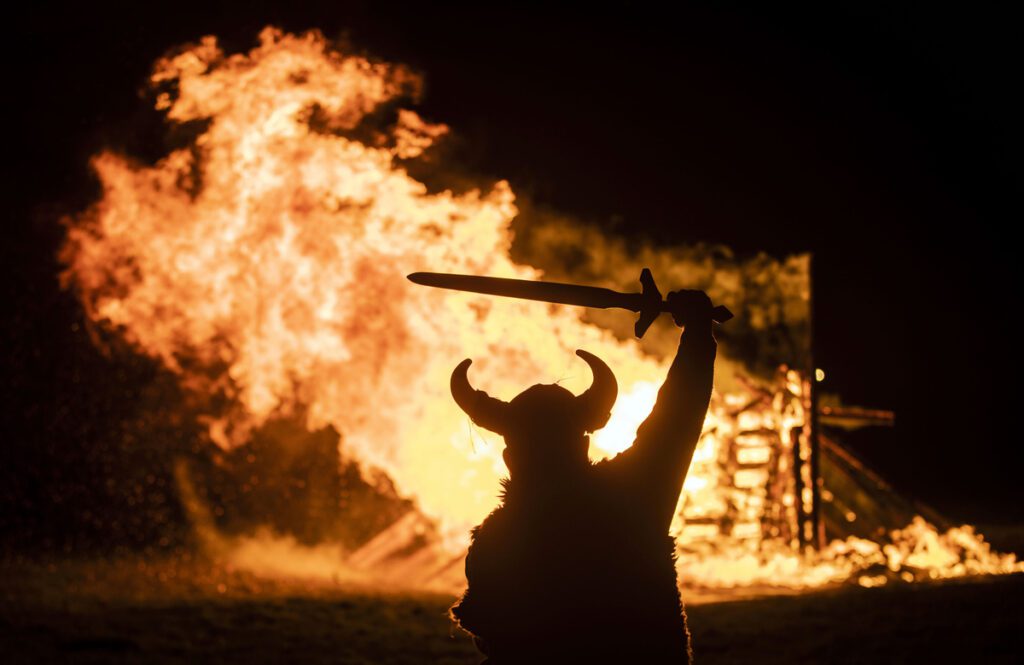 A person in Viking costume in front of a burning Viking boat during the Flamborough Fire Festival, a Viking themed parade, held on New Year's Eve, in Flamborough near Bridlington, Yorkshire.