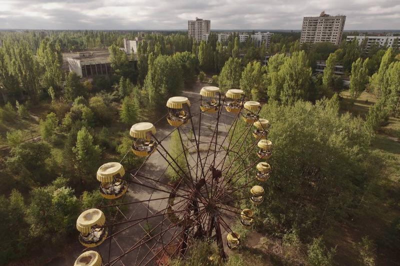In this aerial view an abandoned ferris wheel stands on a public space overgrown with trees in the former city center