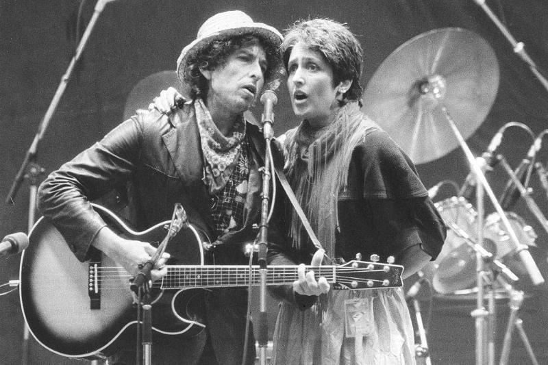 Bob plays guitar while he and Joan sing into a microphone.