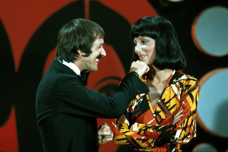 Sonny and Cher grin at one another while onstage.