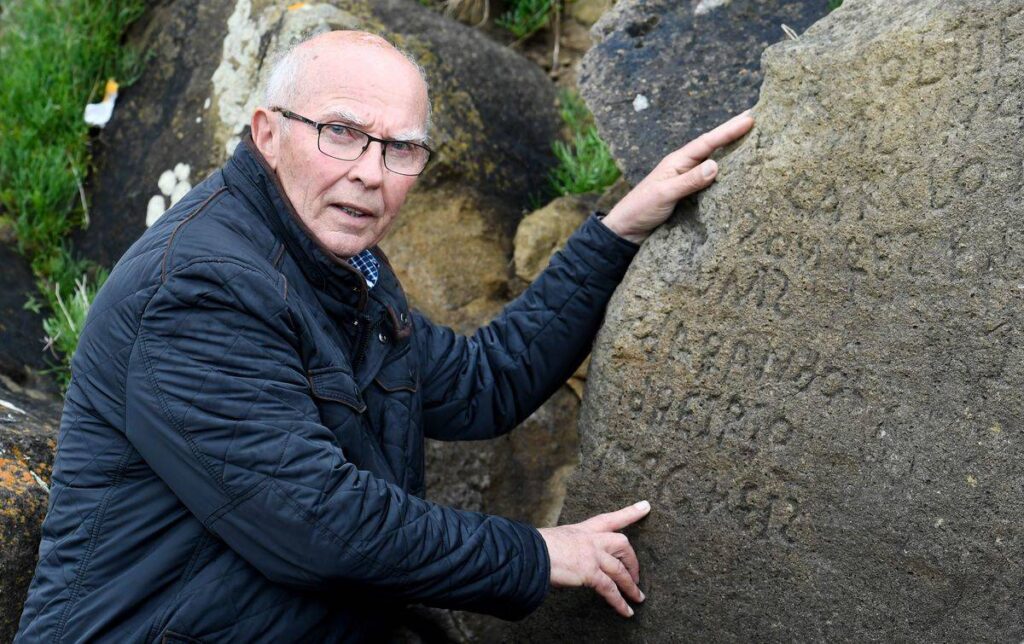 Michel Paugam motions toward inscriptions of the boulder.