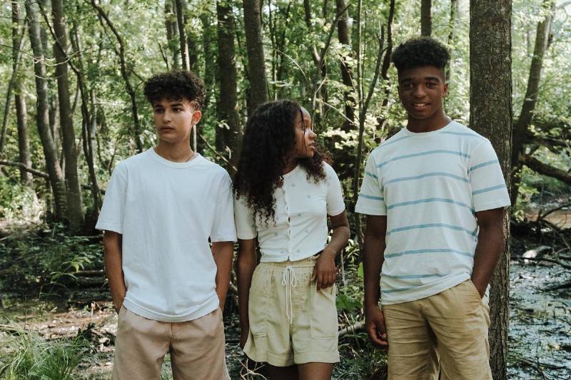 Three teenagers standing in forest.