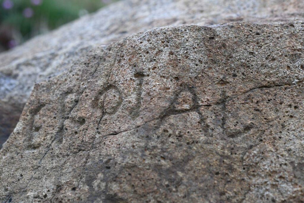 A close-up shot focuses on the boulder's letter engravings.