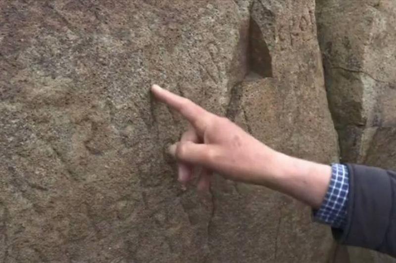 An expert points to some of the engravings on the boulder.