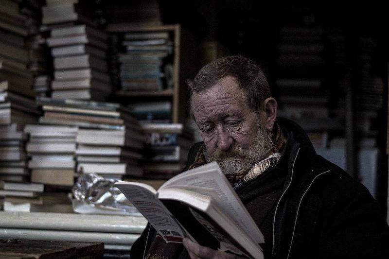 A man reads on book from a large pile.