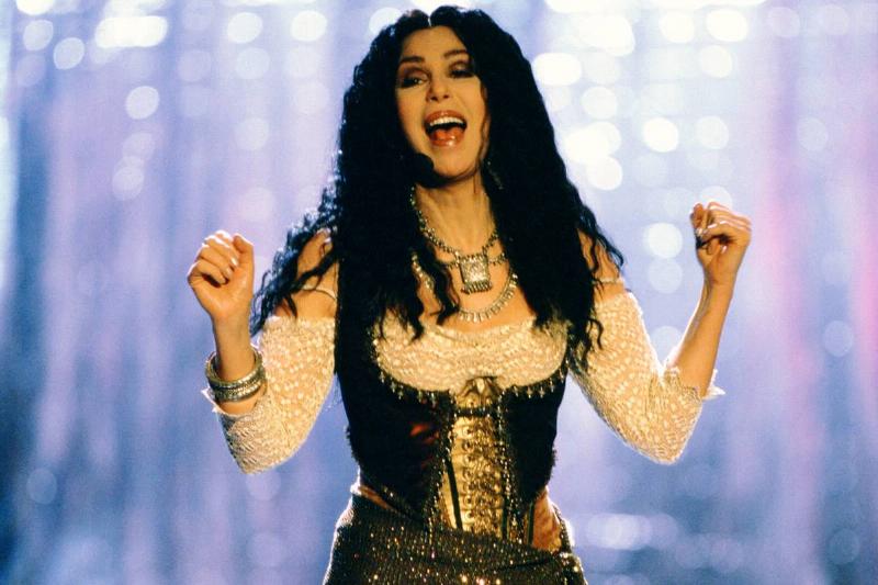 Cher performs onstage in front of glistening lights.