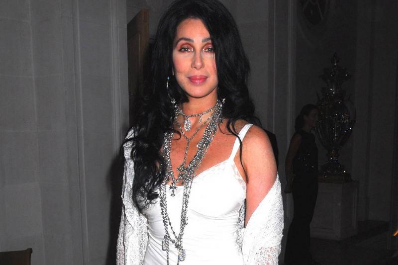 Cher wears a white outfit and thick, silver jewelry.