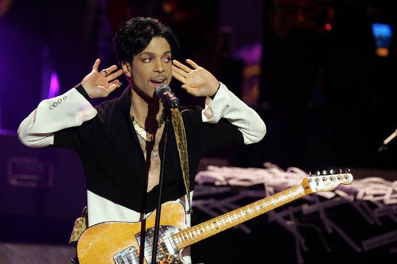 Prince cups his hands around his ears while performing.