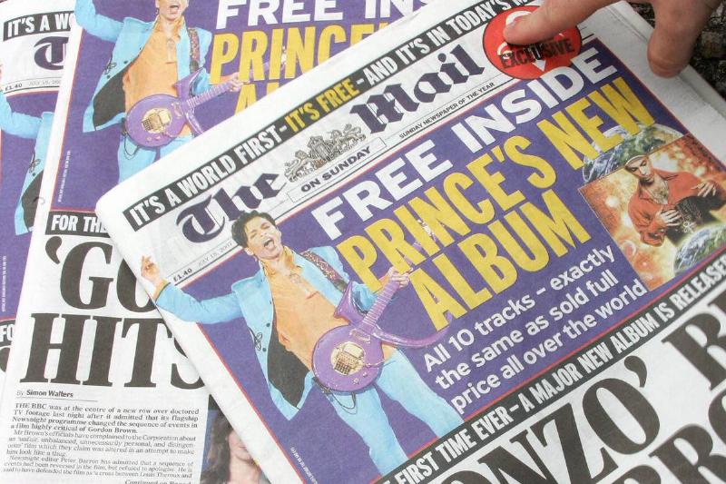 A man picks up a copy of British newspaper The Mail, which includes a copy of the new album by Prince.